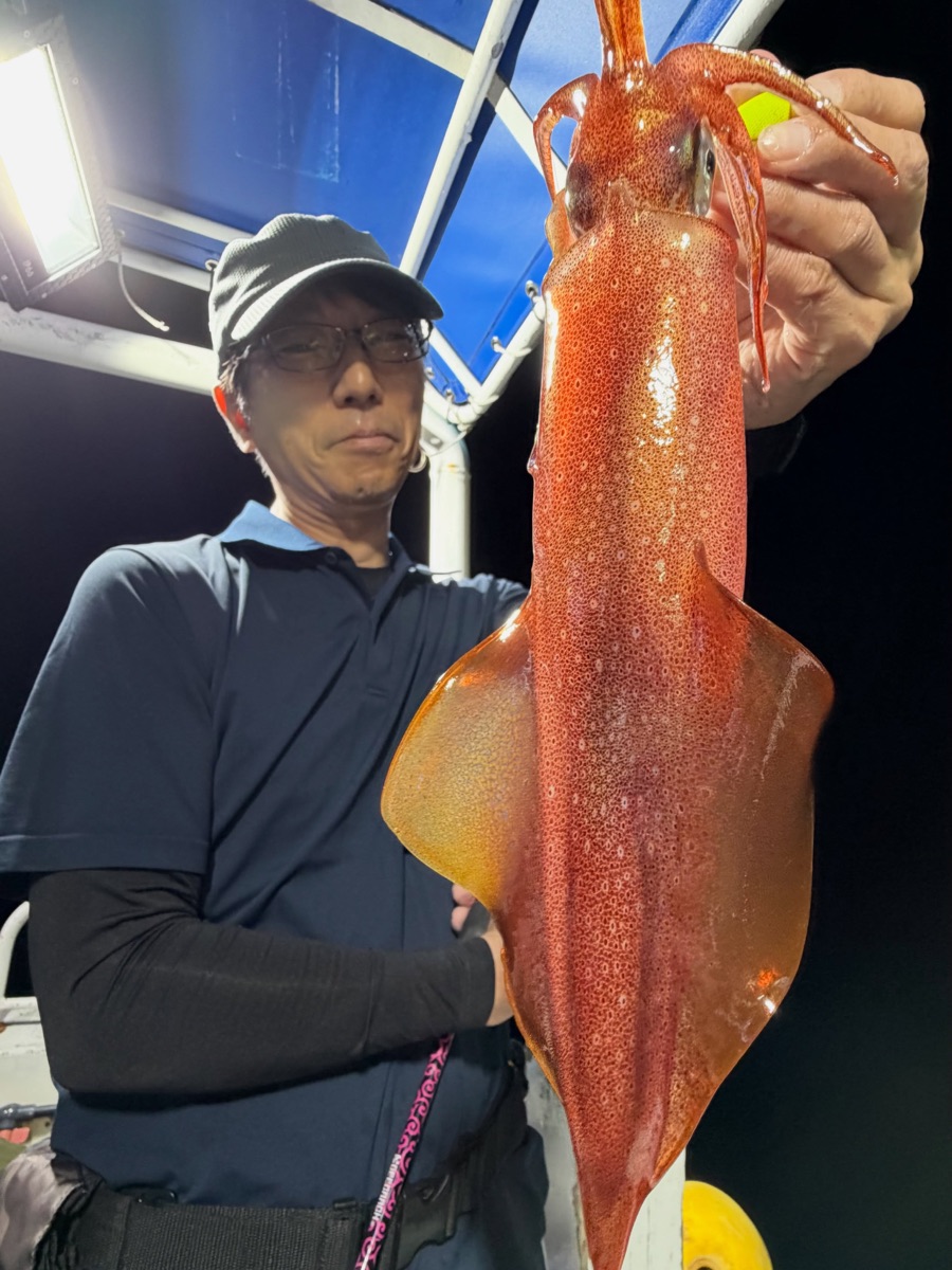夜の船上で、赤みを帯びた大きなマイカを掲げるお客様