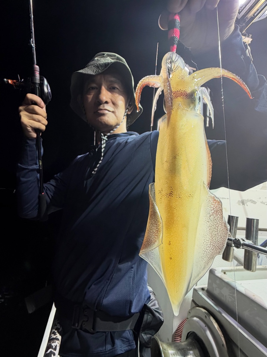 夜の船上で、釣り上げた大きなマイカを掲げるお客様