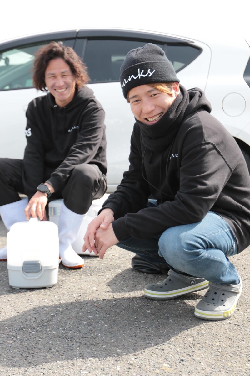 まるまる丸の船長2人。港でしゃがんでこちらを見て笑っている