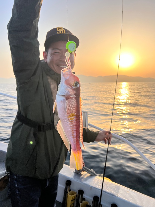 朝日の差す船上で、男性が釣り上げた若狭グジと仕掛けを笑顔で掲げている